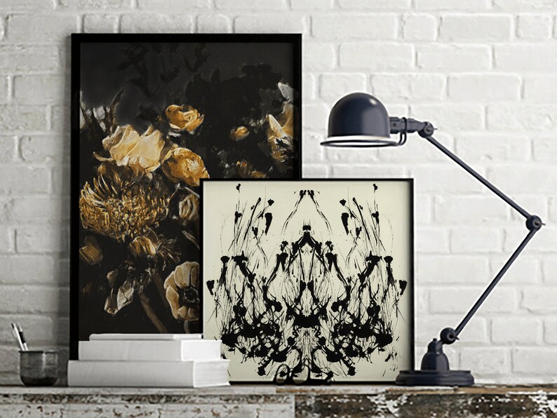 K&ouml;nnte beinhalten: Zwei gerahmte Schwarzwei&szlig;-Abstraktkunst-Drucke mit einer schwarzen Schreibtischlampe vor einem wei&szlig;en Backsteinwand-Hintergrund.