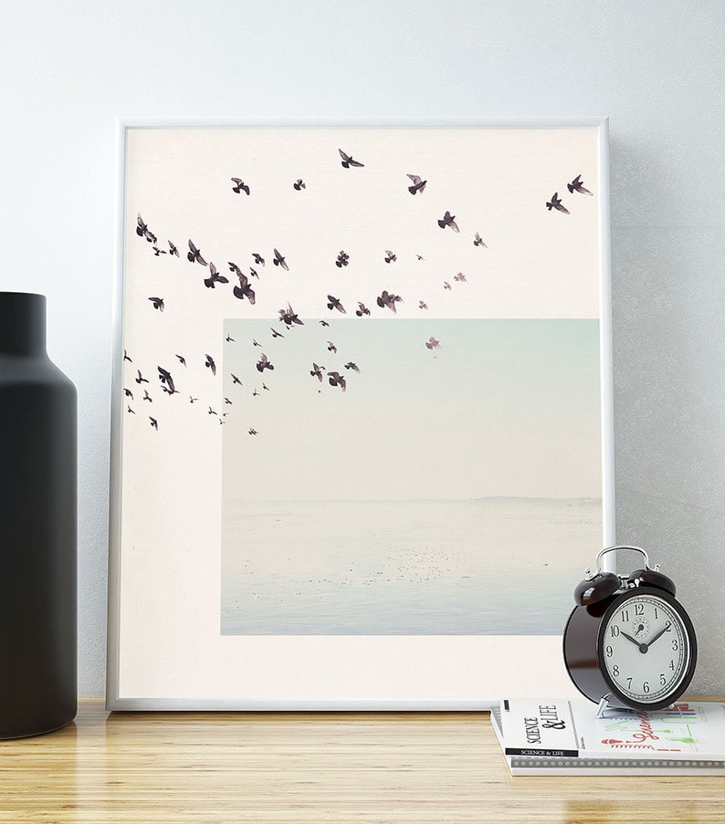 May include: A framed print of a minimalist art piece featuring a flock of black birds flying over a light blue and white landscape.