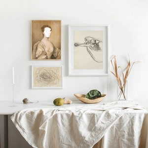 May include: Three framed prints on a white wall above a white table with a white tablecloth. The prints are black and white drawings. The print on the left is a portrait of a woman with a blank face. The print in the middle is a drawing of a tangled mess of lines. The print on the right is a drawing of a person swimming in a pool.