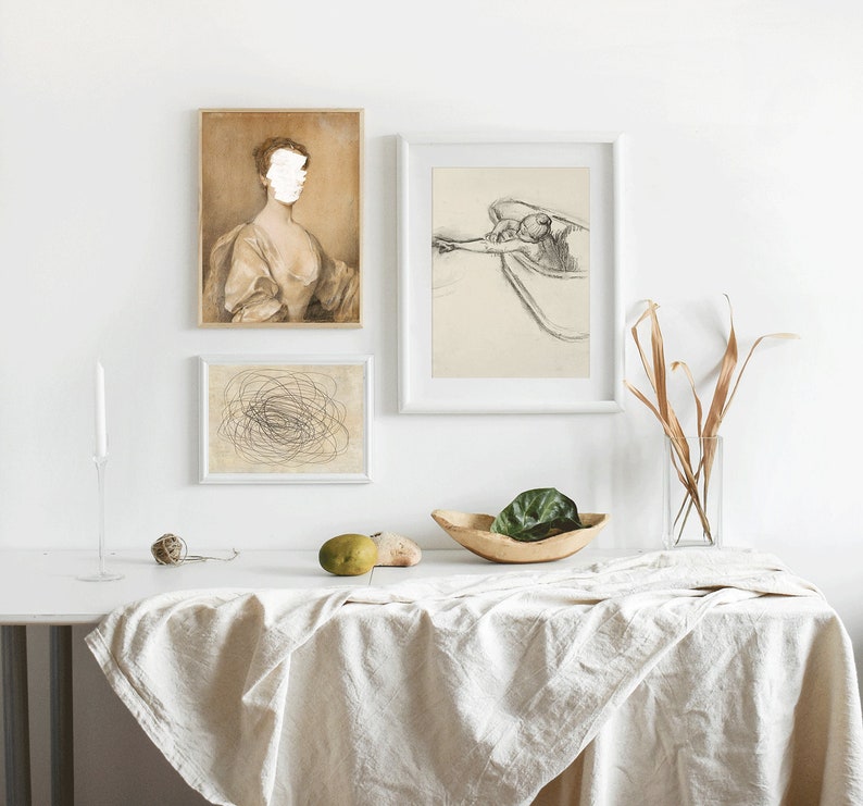 May include: Three framed prints on a white wall above a white table with a white tablecloth. The prints are black and white drawings. The print on the left is a portrait of a woman with a blank face. The print in the middle is a drawing of a tangled mess of lines. The print on the right is a drawing of a person swimming in a pool.