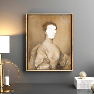 May include: A framed portrait of a woman in a white dress with her face obscured by a white patch. The portrait is set against a gray wall with a gold lamp and decorative objects on a table in the foreground.