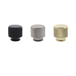 May include: Three cabinet knobs in different finishes: black, nickel, and brass. Each knob has a textured, circular design.