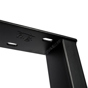 Puede incluir: Primer plano de una pata de mesa de metal negro con una junta soldada. La pata tiene una secci&oacute;n transversal rectangular y est&aacute; estampada con el texto "n.g.".