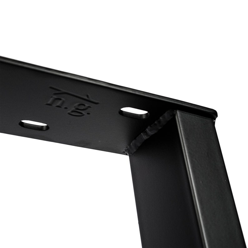 Puede incluir: Primer plano de una pata de mesa de metal negro con una junta soldada. La pata tiene una secci&oacute;n transversal rectangular y est&aacute; estampada con el texto "n.g.".