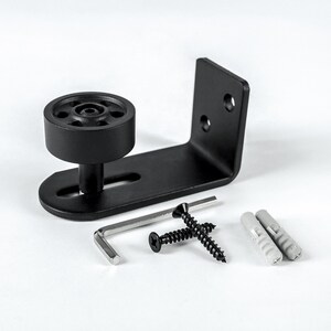 May include: Black metal door floor guide with a wheel, a hex wrench, two screws, and two plastic anchors.