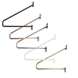 Könnte beinhalten: Fünf Regalhalter in verschiedenen Ausführungen: Schwarz, Kupfer, Silber, Weiß und Gold. Die Halterungen sind aus Metall und haben ein schlichtes, modernes Design.