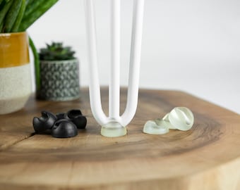 May include: White metal furniture legs with clear plastic floor protectors. There are also black plastic floor protectors in the image.