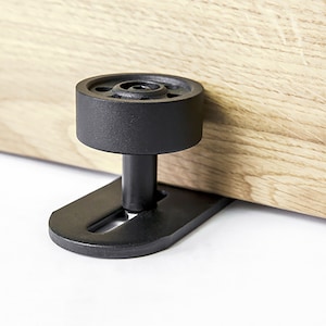 Op de afbeelding: Zwarte metalen schuifdeurrol met een rond wiel en een platte basis. De rol is ontworpen om op een houten deur te worden gemonteerd.