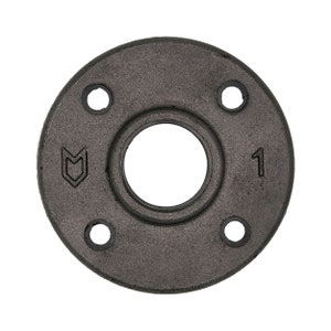 Puede incluir: Una brida de metal negro con cuatro agujeros y un agujero central. La brida tiene un logotipo "M" y el número "1" impreso en ella.