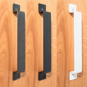 Könnte beinhalten: Drei Türgriffe, einer schwarz, einer weiß und einer dunkelgrau, sind auf einer Holzoberfläche montiert. Jeder Griff hat ein schlichtes, rechteckiges Design mit abgerundeten Kanten.