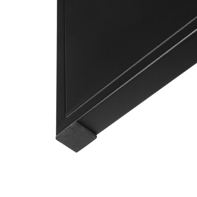 Op de afbeelding: Close-up van een zwarte metalen hoek, mogelijk een tafel of plank. De hoek heeft een rechte hoek met een subtiel verzonken lijndetail. Een klein, vierkant, donkergrijs voetkussen is aan de onderkant bevestigd.