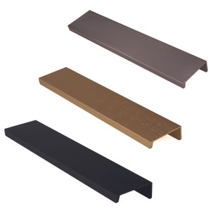 Op de afbeelding: Drie kastgrepen in verschillende afwerkingen: zwart, goud en grijs. Elke greep is rechthoekig met een lichte bocht aan de boven- en onderkant.