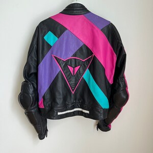 May include: Black leather motorcycle jacket with colorful geometric panels in pink, purple, and turquoise. The jacket has a large Dainese logo on the back.