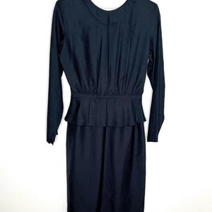 May include: A black long-sleeved dress with a small collar and a peplum waist. The dress is hanging on a white hanger against a white background. The dress has a fitted bodice and a straight skirt.