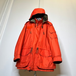 May include: A bright orange hooded jacket with a zipper closure and multiple pockets. The jacket has a drawstring waist and a green lining around the hood.