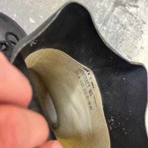 May include: Close-up of the inside of a black rubber boot with a white label that reads "CONTRACT NO. DLA 100-83-C-4110".