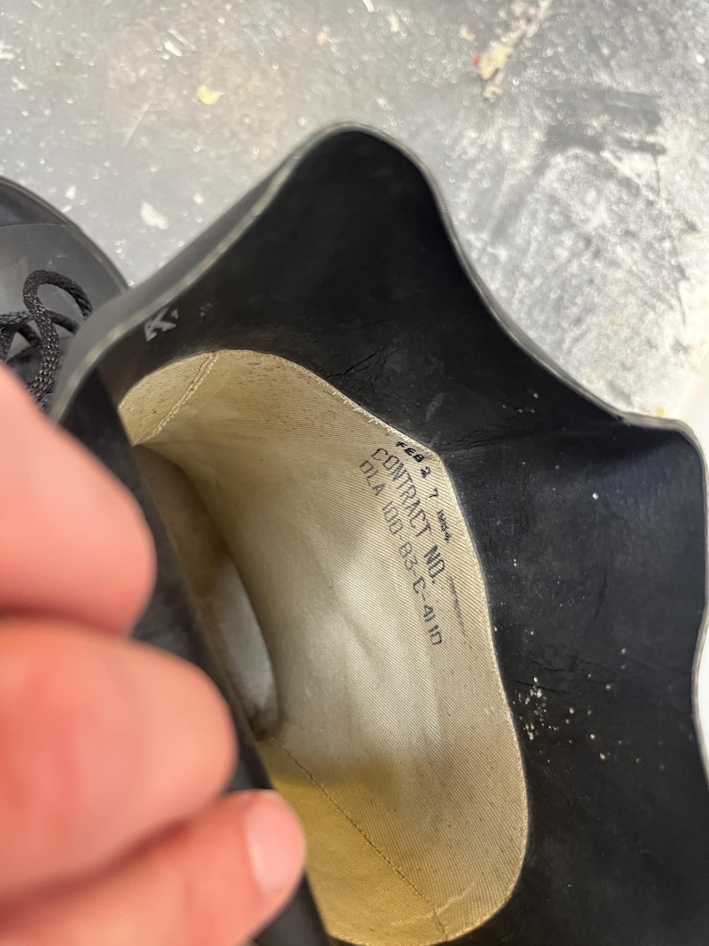 May include: Close-up of the inside of a black rubber boot with a white label that reads "CONTRACT NO. DLA 100-83-C-4110".