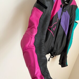 May include: A black leather motorcycle jacket with pink, purple, and teal accents. The jacket has a zipper closure and a stand-up collar.