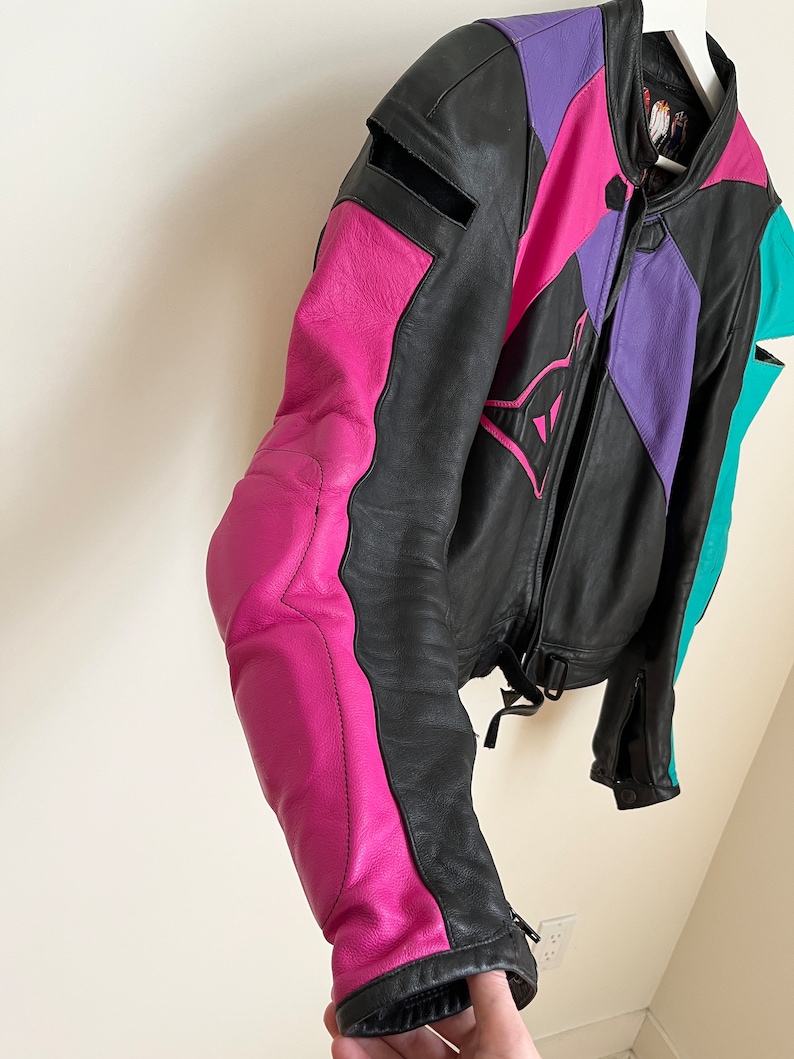 May include: A black leather motorcycle jacket with pink, purple, and teal accents. The jacket has a zipper closure and a stand-up collar.