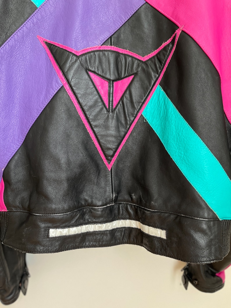 May include: Black leather jacket with pink, purple, and turquoise accents. The jacket features a large triangle logo on the back.