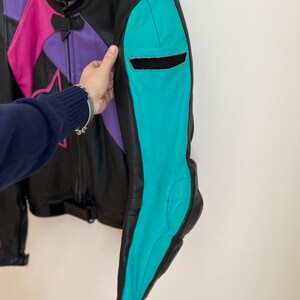 May include: A black leather motorcycle jacket with pink, purple, and turquoise panels. The jacket has a zipper closure and a star design on the front.