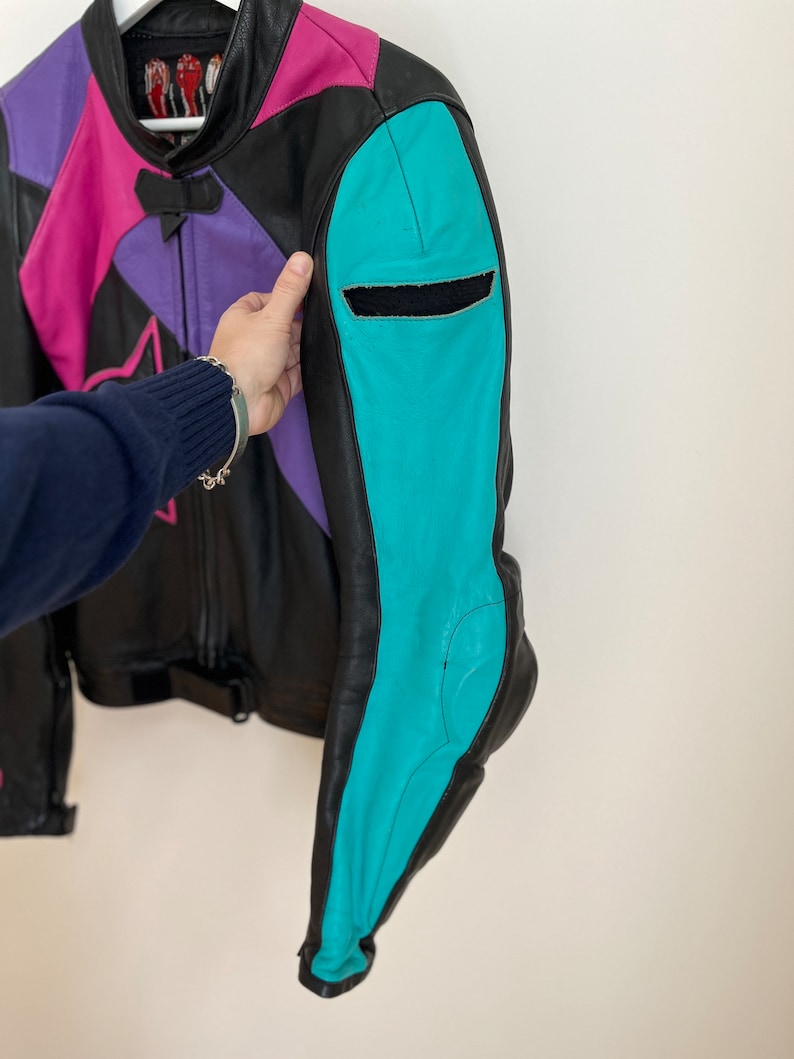 May include: A black leather motorcycle jacket with pink, purple, and turquoise panels. The jacket has a zipper closure and a star design on the front.
