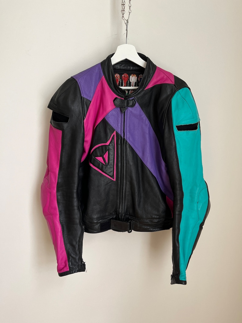 May include: A black leather motorcycle jacket with pink, purple, and turquoise accents. The jacket has a zipper closure and a Dainese logo on the front.