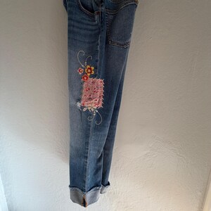 Op de afbeelding: Lichtblauwe spijkerbroek met een bloemenpatch en geborduurde details. De jeans heeft een distressed look met een omgeslagen zoom. De patch heeft roze, gele en rode bloemen.