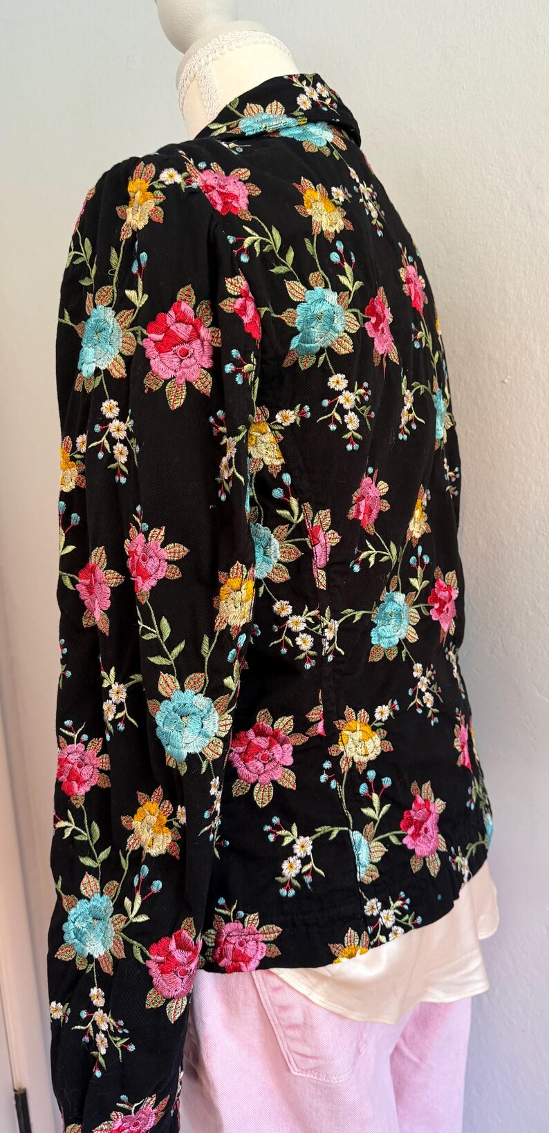 May include: Black jacket with colorful floral embroidery. The jacket features a pattern of pink, red, yellow, and blue flowers with green leaves. The embroidery is detailed and covers the entire jacket.