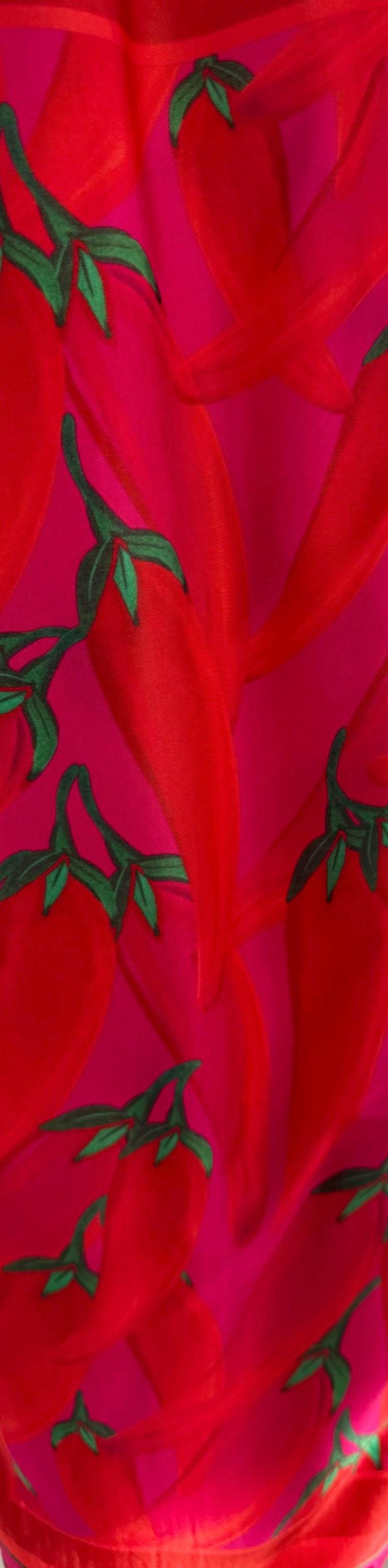 Puede incluir: Un tejido vibrante con un patr&oacute;n repetido de chiles rojos con tallos y hojas verdes sobre un fondo rosa brillante. El dise&ntilde;o es audaz y llamativo, perfecto para ropa o decoraci&oacute;n del hogar.