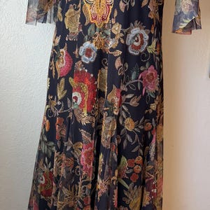 May include: Black floral print dress with sheer sleeves and a gold embroidered neckline. The dress features a long, flowing skirt and a detailed floral pattern in shades of red, yellow, and green.