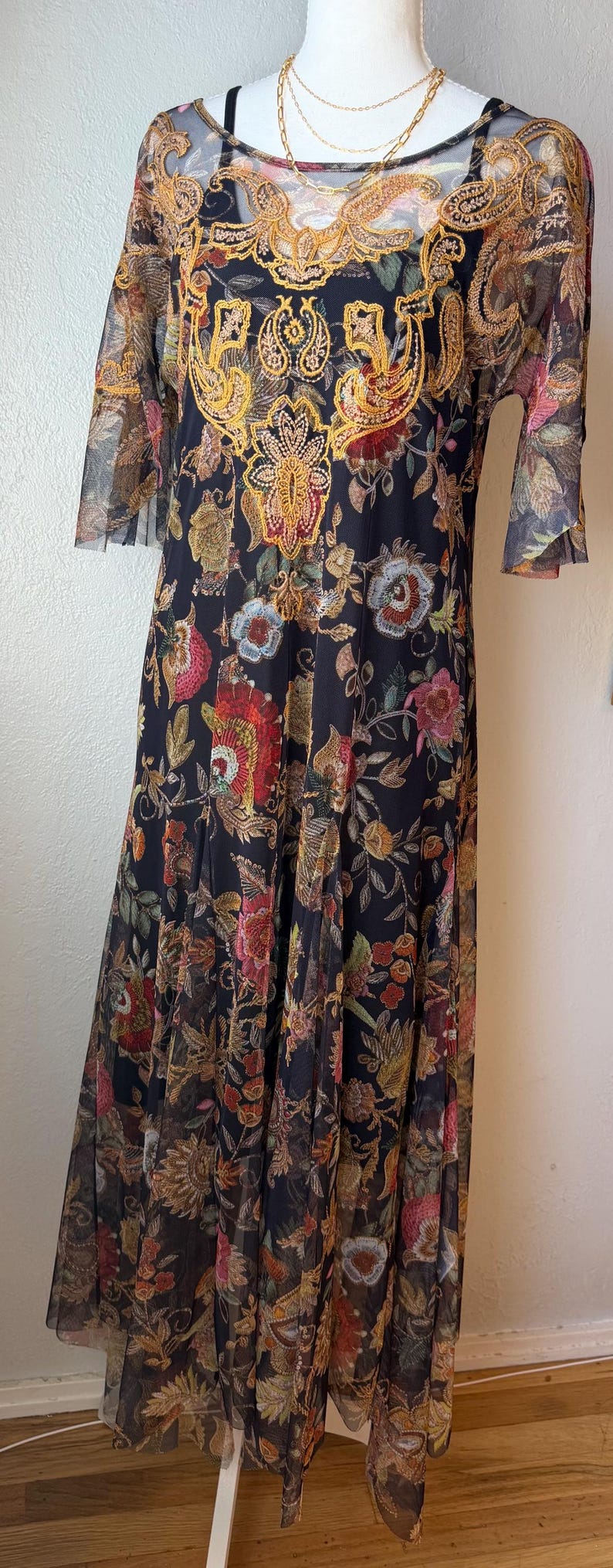 May include: Black floral print dress with sheer sleeves and a gold embroidered neckline. The dress features a long, flowing skirt and a detailed floral pattern in shades of red, yellow, and green.