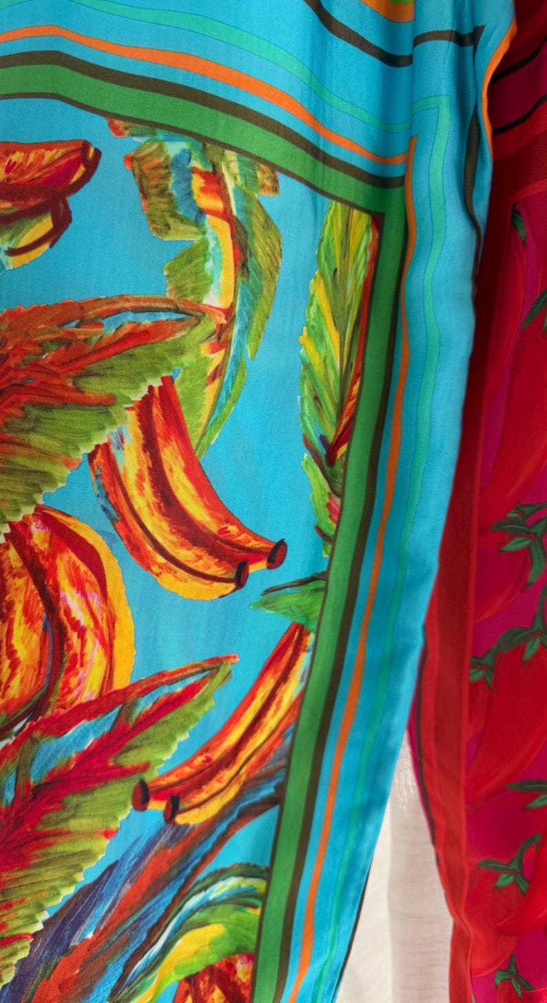 Puede incluir: Un textil vibrante con un estampado de pl&aacute;tanos coloridos sobre un fondo azul claro. El dise&ntilde;o incluye pl&aacute;tanos rojos, amarillos y naranjas con hojas verdes. Un borde a rayas en verde, naranja y marr&oacute;n enmarca el dise&ntilde;o. A la derecha se ve una tela roja con estampado de chiles.