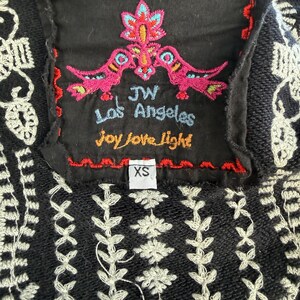 K&ouml;nnte beinhalten: Schwarz besticktes Oberteil mit wei&szlig;en Blumen- und geometrischen Mustern. Ein schwarzes Etikett zeigt farbenfrohe Stickereien von V&ouml;geln und Blumen mit dem Text "JW Los Angeles Joy Love Light". Das Gr&ouml;&szlig;enetikett lautet "XS".