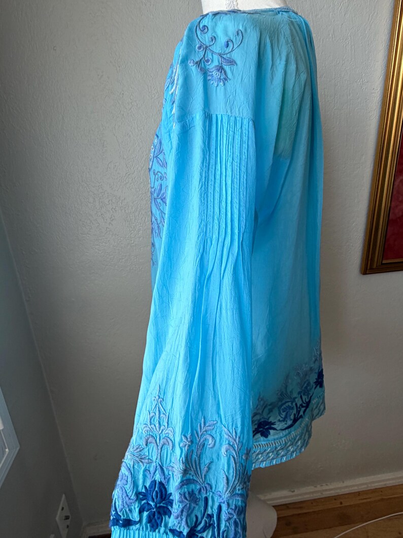 Puede incluir: Blusa azul claro de manga larga con intrincados bordados florales en tonos azules. La blusa presenta detalles plisados en las mangas y pu&ntilde;os, y un ajuste holgado y relajado. El bordado a&ntilde;ade un toque de elegancia al estilo casual.