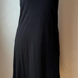 May include: A black slip dress with spaghetti straps is displayed on a white mannequin. A gold-colored layered necklace is draped around the mannequin's neck. The dress has a simple, classic design.