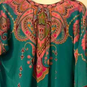 May include: A teal-colored top with a vibrant paisley pattern in pink, orange, and green. The top features a round neckline and long sleeves. The intricate design includes floral and teardrop motifs.