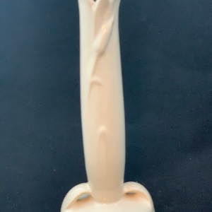 May include: A tall, slender, off-white ceramic bud vase with a smooth, glossy finish. The vase features a stylized, molded floral design that extends upward along the body, culminating in a flared, petal-like rim and a circular base.