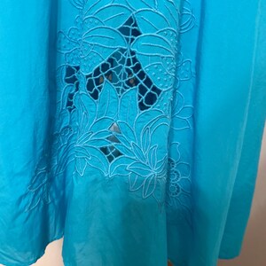 Puede incluir: Una vibrante tela turquesa con un dise&ntilde;o floral calado. El intrincado patr&oacute;n presenta hojas y p&eacute;talos detallados, agregando un toque delicado al textil. La tela est&aacute; drapeada, mostrando su textura fluida y el juego de luces y sombras.