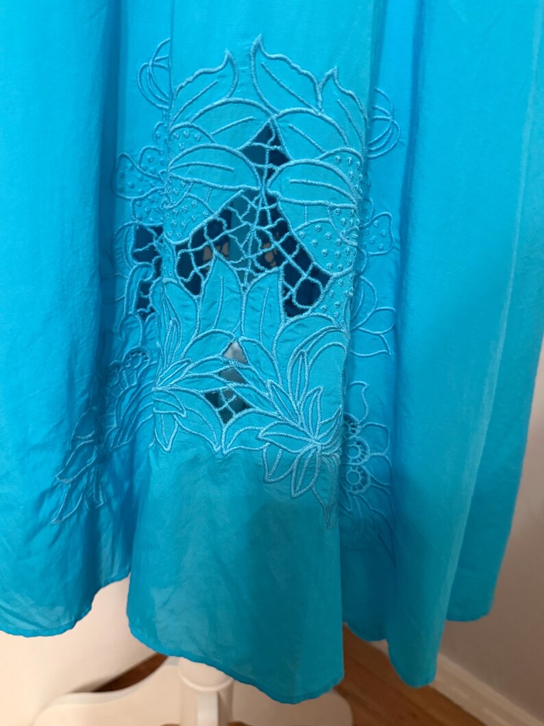 Puede incluir: Una vibrante tela turquesa con un dise&ntilde;o floral calado. El intrincado patr&oacute;n presenta hojas y p&eacute;talos detallados, agregando un toque delicado al textil. La tela est&aacute; drapeada, mostrando su textura fluida y el juego de luces y sombras.