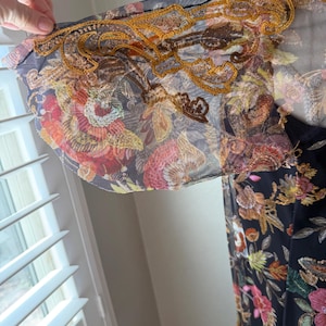May include: A black dress with a floral pattern featuring red, pink, and yellow flowers. The sleeves are sheer with gold embroidery along the edges. The dress is made of a lightweight fabric.