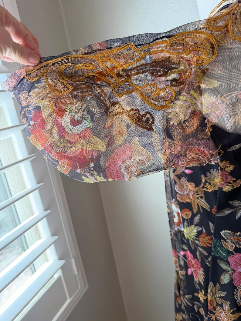 May include: A black dress with a floral pattern featuring red, pink, and yellow flowers. The sleeves are sheer with gold embroidery along the edges. The dress is made of a lightweight fabric.