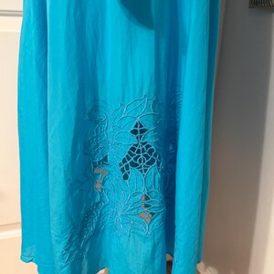 Puede incluir: Un vestido turquesa vibrante con un dise&ntilde;o floral recortado cerca del dobladillo. El vestido parece estar hecho de una tela ligera, adecuada para climas c&aacute;lidos. El patr&oacute;n recortado a&ntilde;ade un elemento decorativo a la prenda.