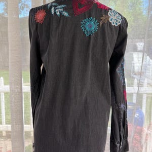 以下が含まれることがあります： 背中と袖にカラフルな花の刺繍が施された黒のデニムシャツ。 シャツは長袖、ほつれた裾、ボタンダウンフロントです。 刺繍には、赤、青、ピンクの花と赤いハートが含まれています。