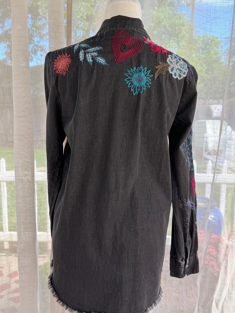 以下が含まれることがあります： 背中と袖にカラフルな花の刺繍が施された黒のデニムシャツ。 シャツは長袖、ほつれた裾、ボタンダウンフロントです。 刺繍には、赤、青、ピンクの花と赤いハートが含まれています。