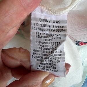 May include: A white fabric tag with the brand name "JOHNNY WAS" and address details. The tag also lists the style, material composition, and care instructions, including "MACHINE WASH COLD" and "TUMBLE DRY LOW".