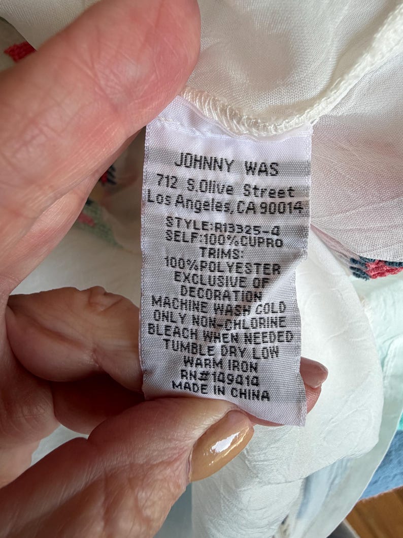 May include: A white fabric tag with the brand name "JOHNNY WAS" and address details. The tag also lists the style, material composition, and care instructions, including "MACHINE WASH COLD" and "TUMBLE DRY LOW".