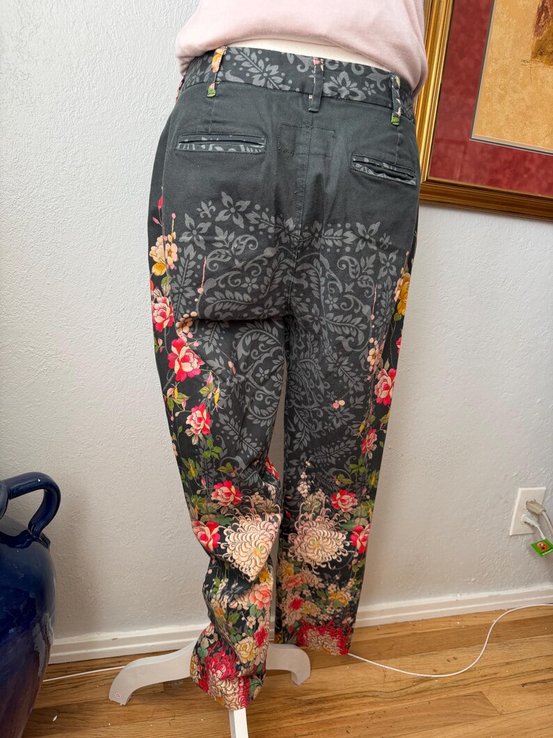 Puede incluir: Pantalones gris carb&oacute;n oscuro con un patr&oacute;n de damasco negro en la parte superior y estampados florales vibrantes en tonos rojo, rosa, amarillo y verde en la parte inferior de las piernas, con dos bolsillos traseros y cinturilla.