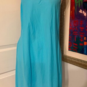 Puede incluir: Un vestido lencero turquesa con finas tiras de espagueti. El vestido se exhibe en un maniqu&iacute;. La tela parece ligera y tiene un ligero brillo. El vestido llega hasta la rodilla.