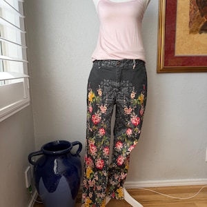 Puede incluir: Una camiseta de tirantes rosa p&aacute;lido combinada con pantalones gris oscuro con un estampado floral de rosas rojas, amarillas y rosas. Los pantalones tienen una cintura gris oscuro y un patr&oacute;n intrincado que se repite en la tela.
